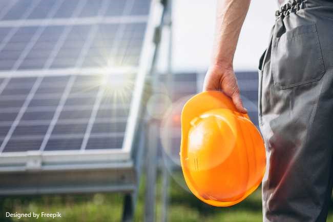 Panel solar de fondo con destello de sol, casco de trabajo y brazo y pierna de persona, un técnico que va a comprobar el panel